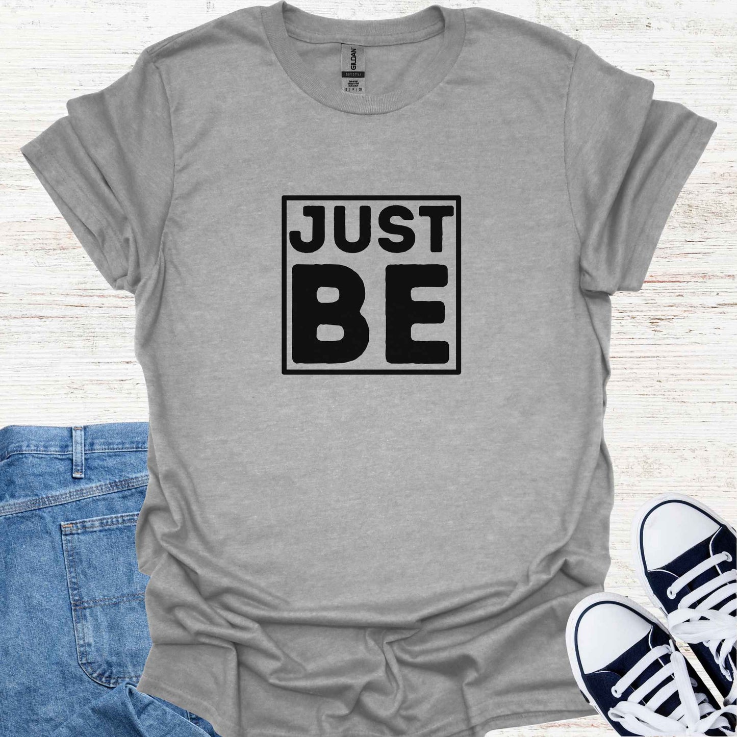 Grey t-shirt design featuring the minimalist phrase 'Just Be' in bold typography, framed for emphasis. The design conveys a profound spiritual message about living in the present moment, embracing simplicity, and finding peace in existence itself. It encourages mindfulness, acceptance, and the art of simply being, free from the need to do or become anything. Perfect for those drawn to spirituality, introspection, and mindful living.