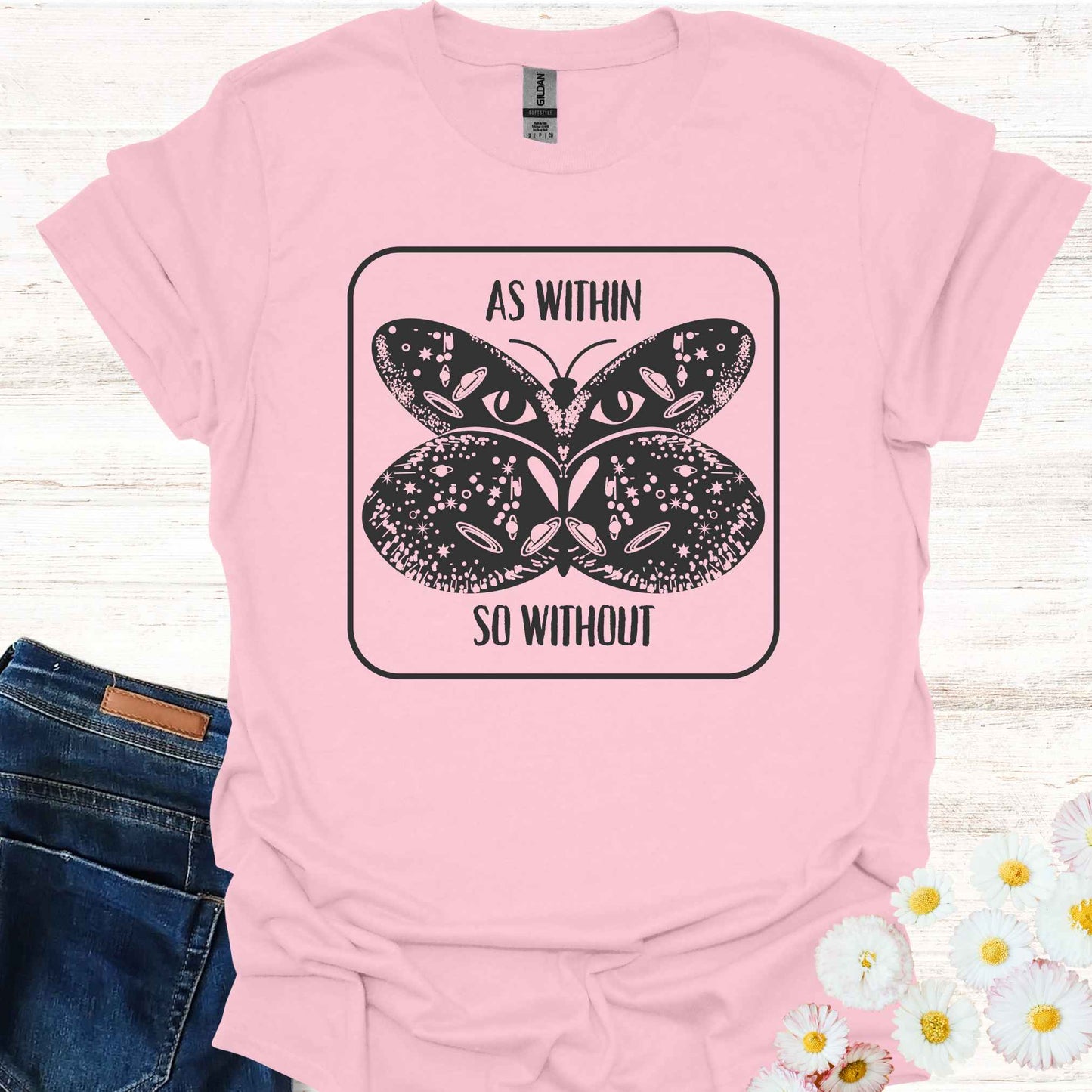 Light pink t-shirt featuring a detailed graphic of a butterfly with cosmic and universal symbols on its wings, paired with the philosophical phrase 'As Within So Without.' This design reflects the idea that the external world is a reflection of our inner selves, symbolizing the interconnectedness of the universe and our own universal consciousness.