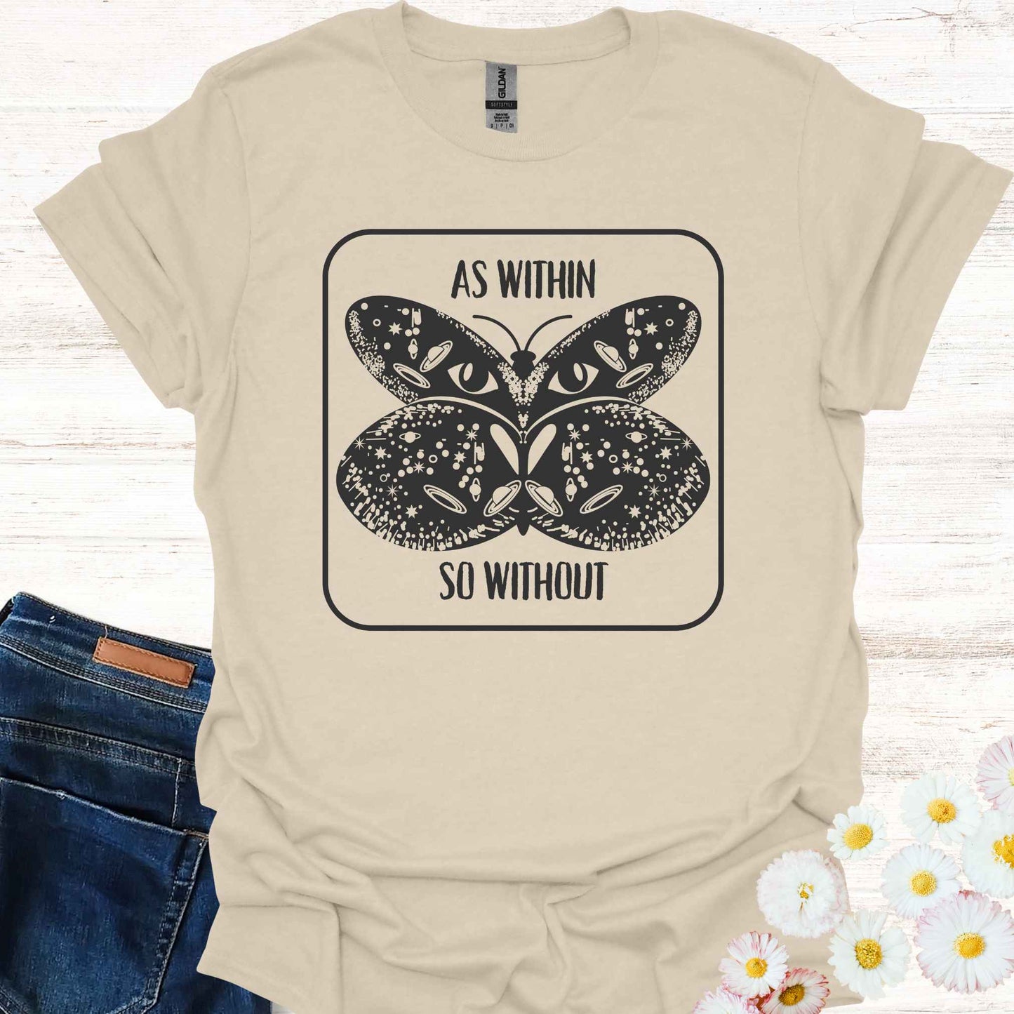 Beige t-shirt featuring a detailed graphic of a butterfly with cosmic and universal symbols on its wings, paired with the philosophical phrase 'As Within So Without.' This design reflects the idea that the external world is a reflection of our inner selves, symbolizing the interconnectedness of the universe and our own universal consciousness.