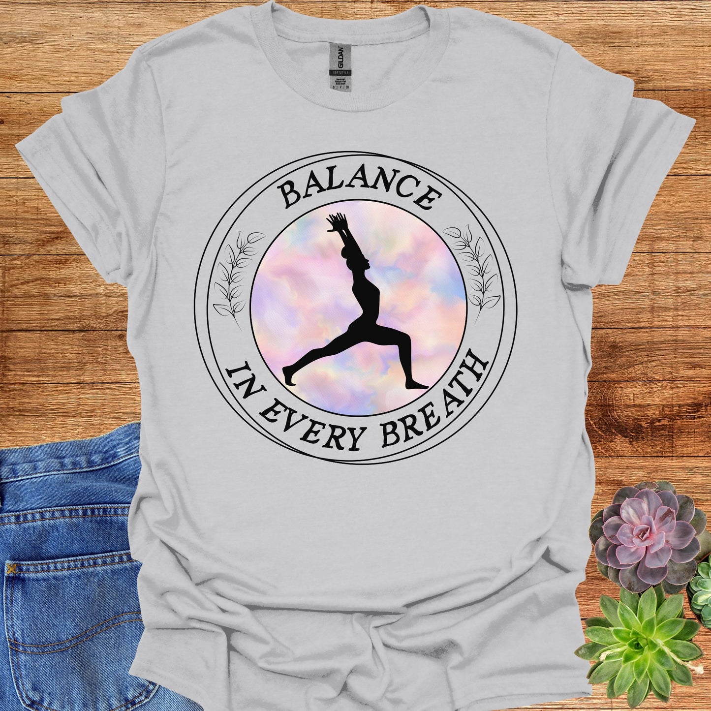 Grey t-shirt featuring a round frame enclosing the silhouette of a person in a yoga pose, surrounded by the phrase 'Balance in Every Breath.' This design embodies the yogic teaching of cultivating awareness in both movement and breath, promoting mindfulness, harmony, and inner peace. Ideal for yoga enthusiasts and those seeking balance and calm in their daily lives.