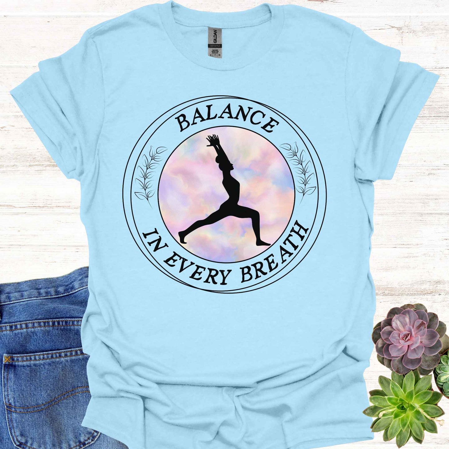 Light blue t-shirt featuring a round frame enclosing the silhouette of a person in a yoga pose, surrounded by the phrase 'Balance in Every Breath.' This design embodies the yogic teaching of cultivating awareness in both movement and breath, promoting mindfulness, harmony, and inner peace. Ideal for yoga enthusiasts and those seeking balance and calm in their daily lives.