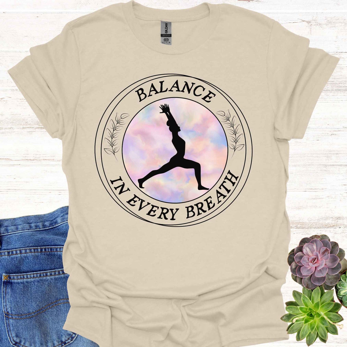 Beige t-shirt featuring a round frame enclosing the silhouette of a person in a yoga pose, surrounded by the phrase 'Balance in Every Breath.' This design embodies the yogic teaching of cultivating awareness in both movement and breath, promoting mindfulness, harmony, and inner peace. Ideal for yoga enthusiasts and those seeking balance and calm in their daily lives.