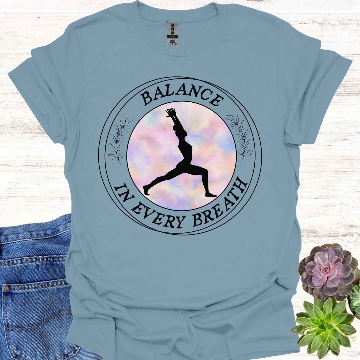 Blue t-shirt featuring a round frame enclosing the silhouette of a person in a yoga pose, surrounded by the phrase 'Balance in Every Breath.' This design embodies the yogic teaching of cultivating awareness in both movement and breath, promoting mindfulness, harmony, and inner peace. Ideal for yoga enthusiasts and those seeking balance and calm in their daily lives.