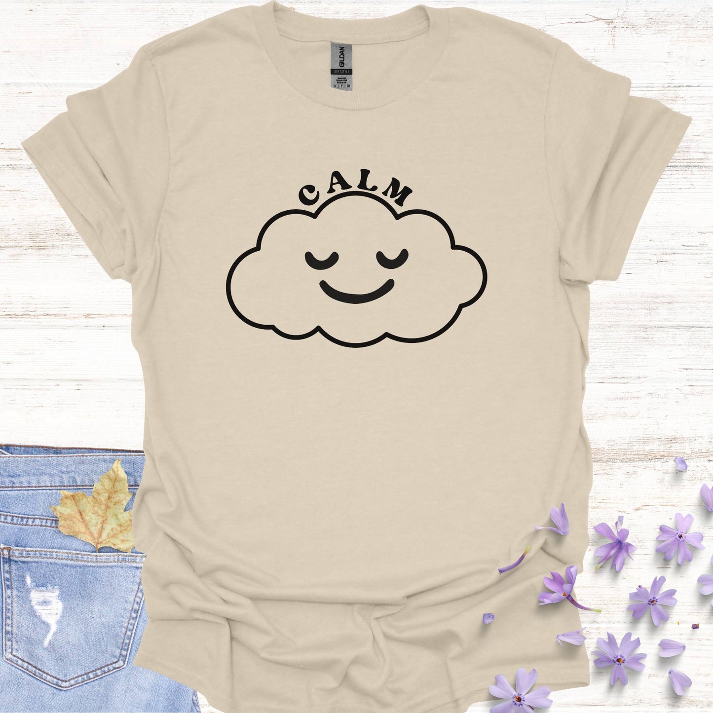 Beige t-shirt featuring design of a minimalist line drawing of a cloud with a serene smiling face inside, accompanied by the word "calm" in bold typography. This design symbolizes inner peace, tranquility, and emotional balance, reminding wearers to embrace calmness in the midst of life's challenges. Perfect for the personal growth enthusiasts, it inspires mindfulness, self-reflection, and a sense of ease.