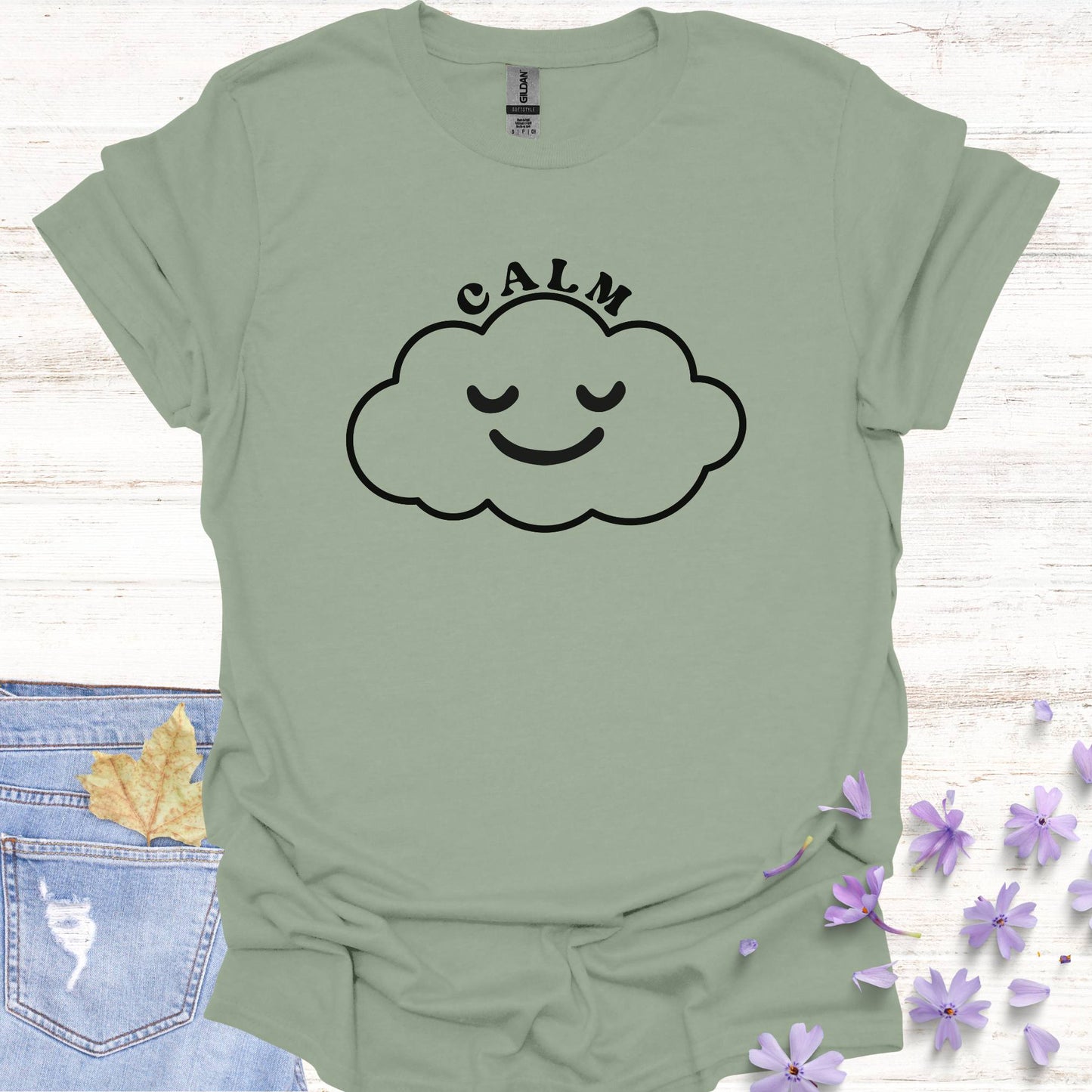 Sage green t-shirt featuring design of a minimalist line drawing of a cloud with a serene smiling face inside, accompanied by the word "calm" in bold typography. This design symbolizes inner peace, tranquility, and emotional balance, reminding wearers to embrace calmness in the midst of life's challenges. Perfect for the personal growth enthusiasts, it inspires mindfulness, self-reflection, and a sense of ease.