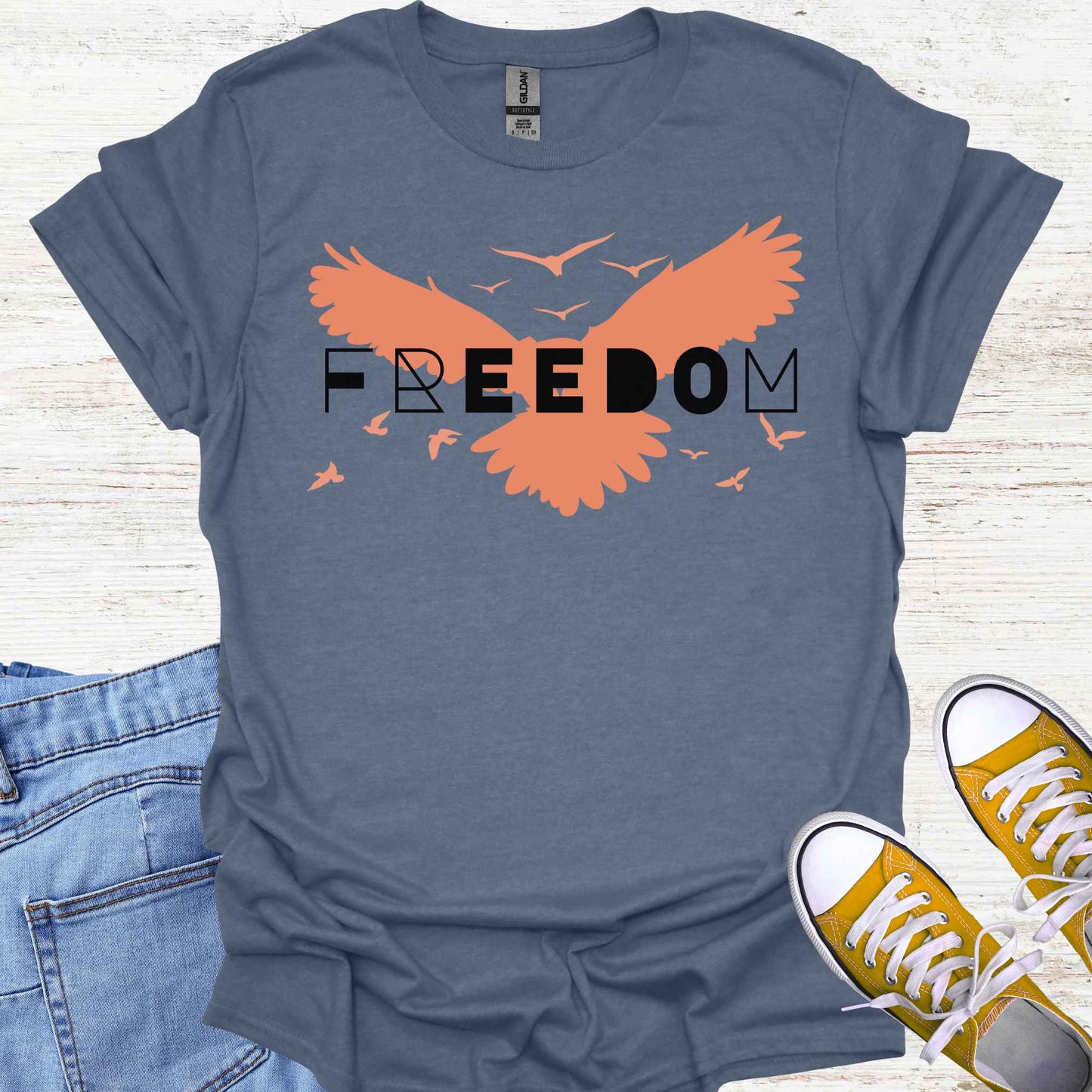 Blue t-shirt featuring an orange bird with its wings spread, symbolizing freedom and liberation, with the bold word 'FREEDOM' in stylish typography placed on top. This design evokes the spirit of independence, self-expression, and the boundless potential of the human soul, inspired by the free flight of birds.