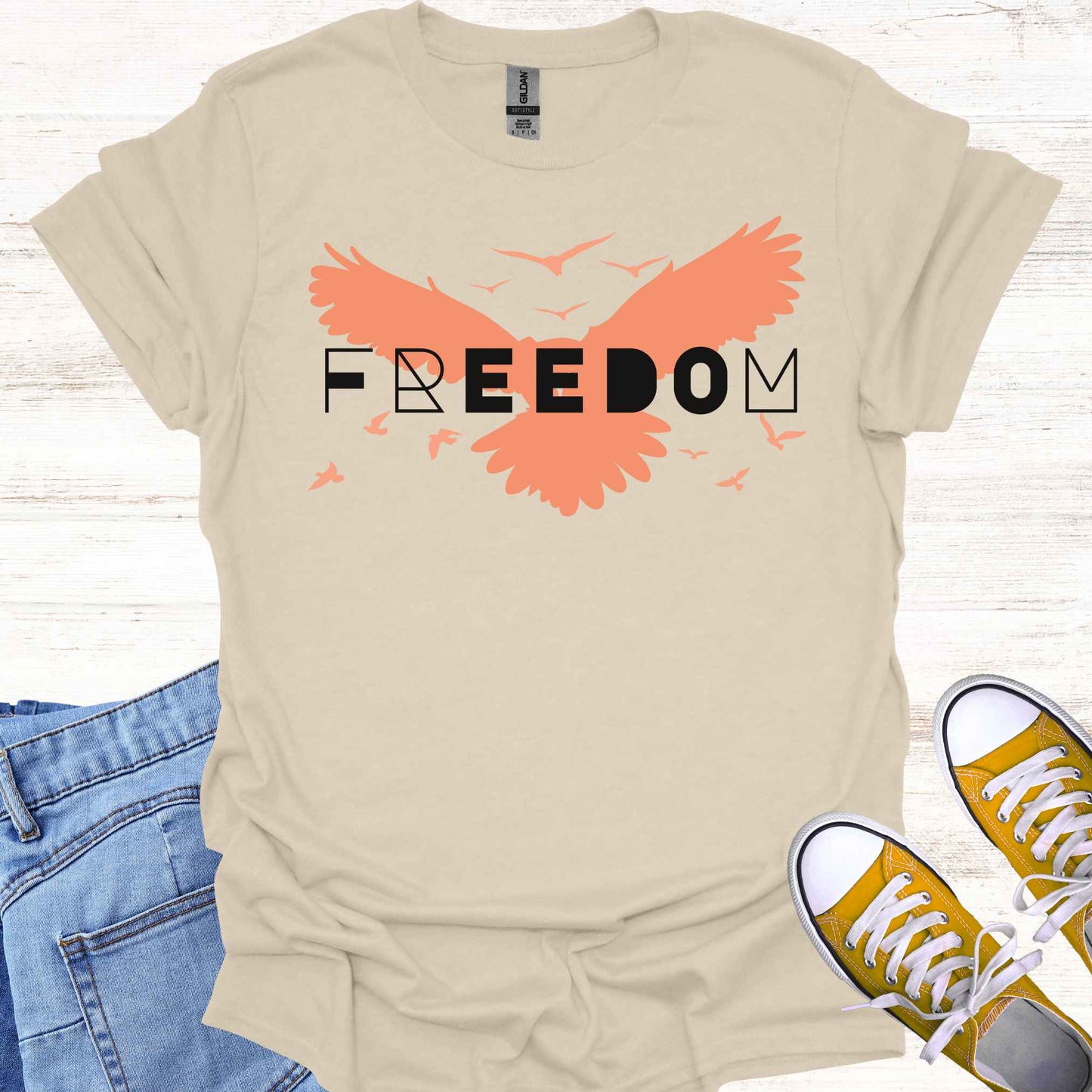 Beige t-shirt featuring an orange bird with its wings spread, symbolizing freedom and liberation, with the bold word 'FREEDOM' in stylish typography placed on top. This design evokes the spirit of independence, self-expression, and the boundless potential of the human soul, inspired by the free flight of birds.