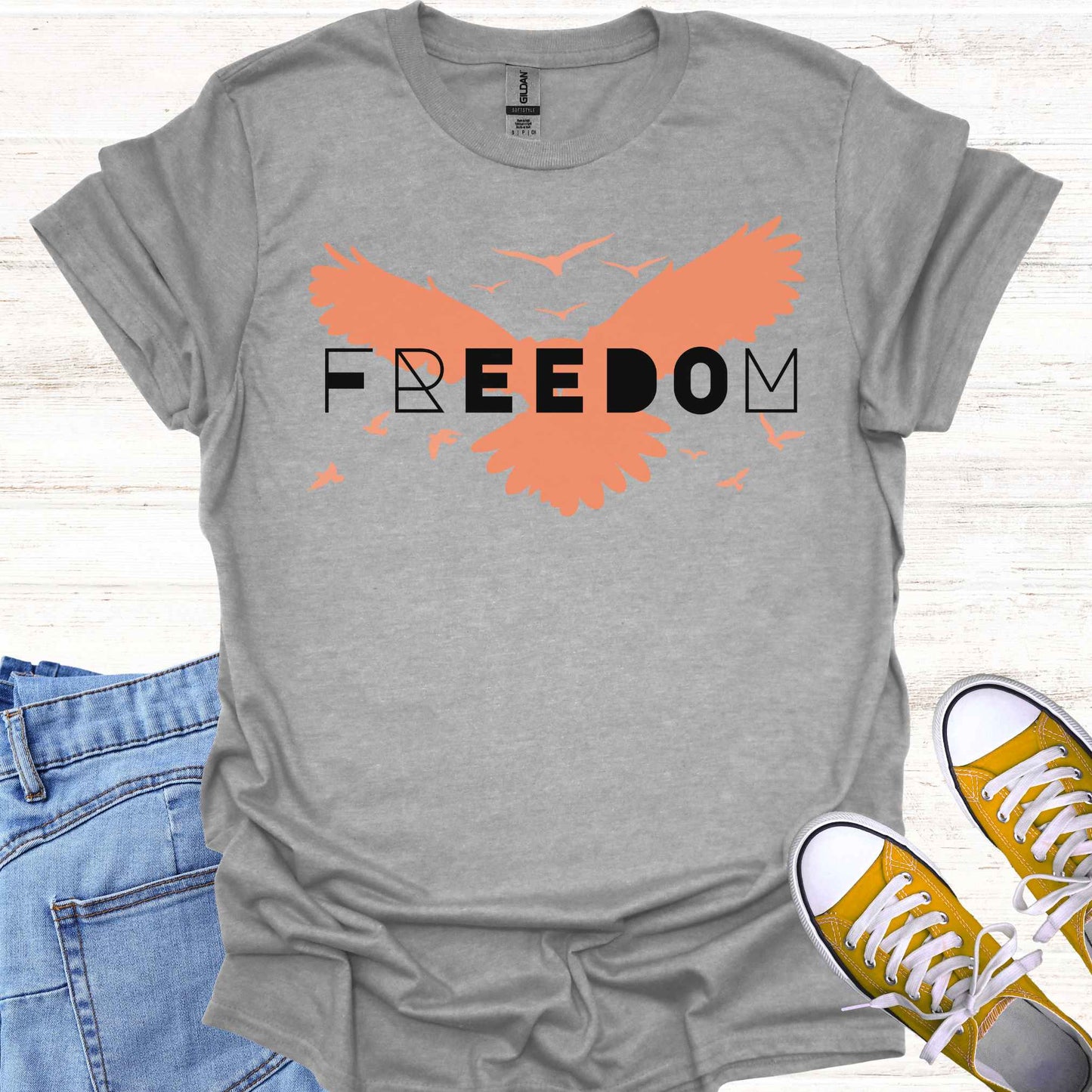 Grey t-shirt featuring an orange bird with its wings spread, symbolizing freedom and liberation, with the bold word 'FREEDOM' in stylish typography placed on top. This design evokes the spirit of independence, self-expression, and the boundless potential of the human soul, inspired by the free flight of birds.