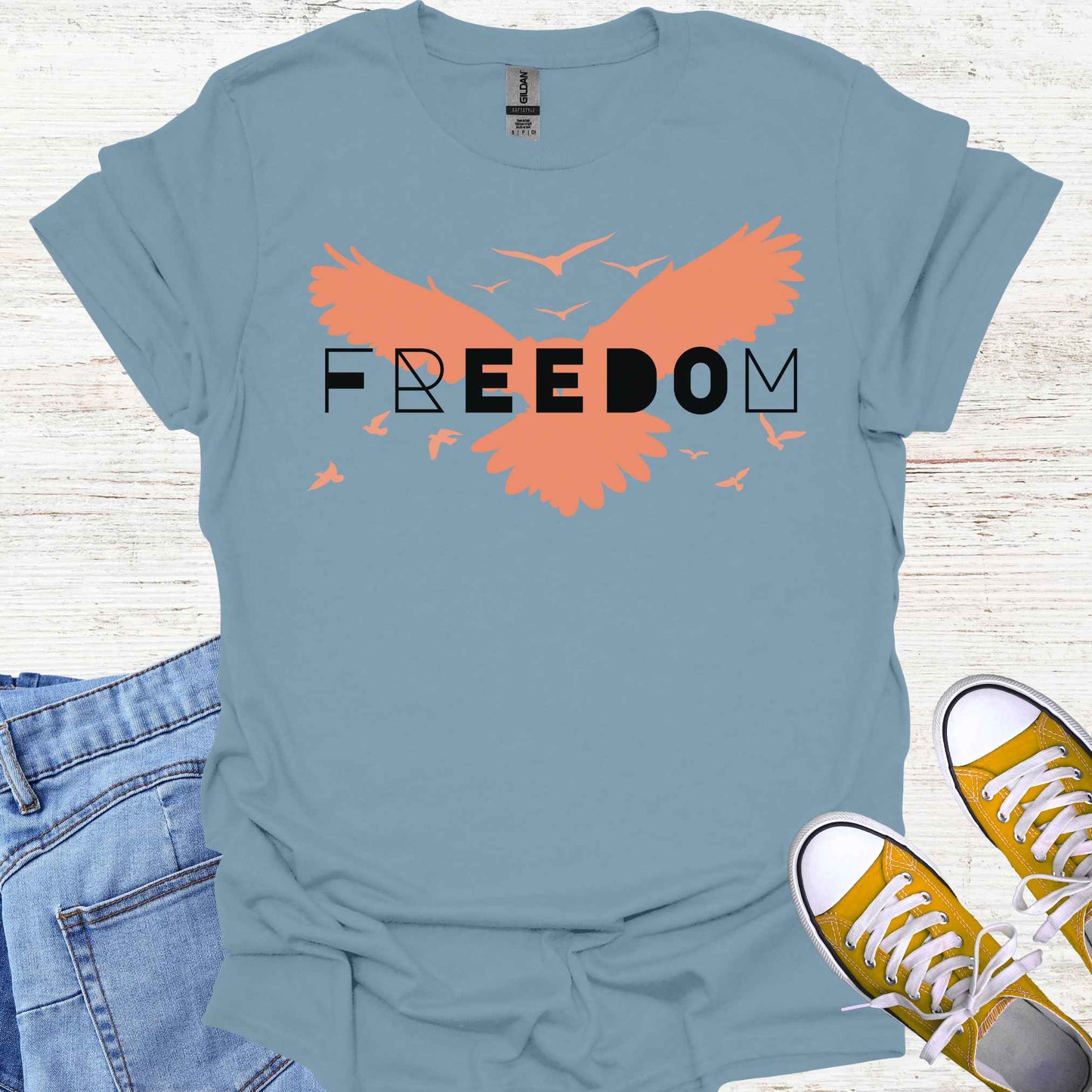 Blue t-shirt featuring an orange bird with its wings spread, symbolizing freedom and liberation, with the bold word 'FREEDOM' in stylish typography placed on top. This design evokes the spirit of independence, self-expression, and the boundless potential of the human soul, inspired by the free flight of birds.