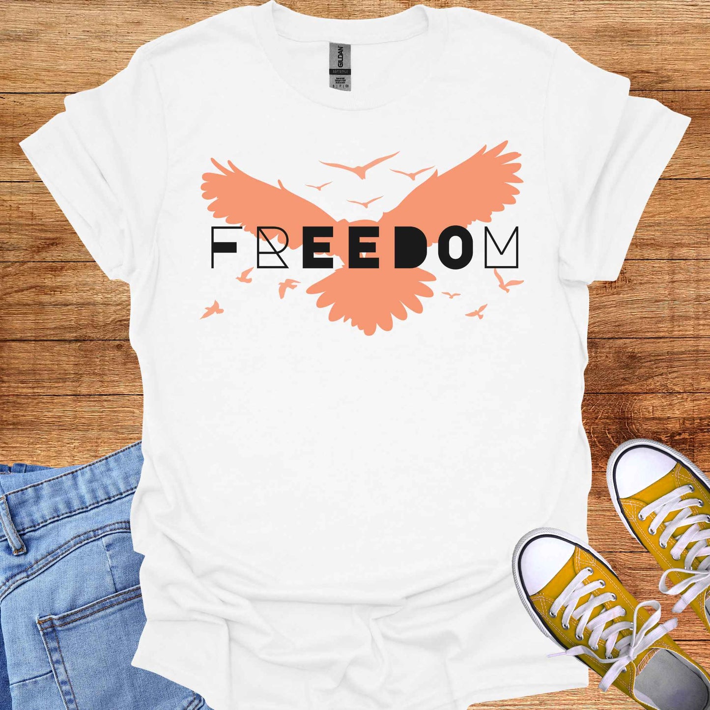 White t-shirt featuring an orange bird with its wings spread, symbolizing freedom and liberation, with the bold word 'FREEDOM' in stylish typography placed on top. This design evokes the spirit of independence, self-expression, and the boundless potential of the human soul, inspired by the free flight of birds.