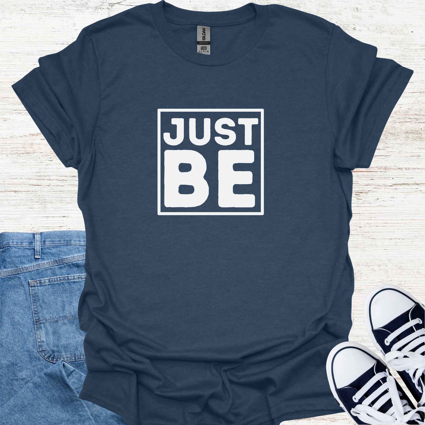Blue t-shirt design featuring the minimalist phrase 'Just Be' in bold typography, framed for emphasis. The design conveys a profound spiritual message about living in the present moment, embracing simplicity, and finding peace in existence itself. It encourages mindfulness, acceptance, and the art of simply being, free from the need to do or become anything. Perfect for those drawn to spirituality, introspection, and mindful living.