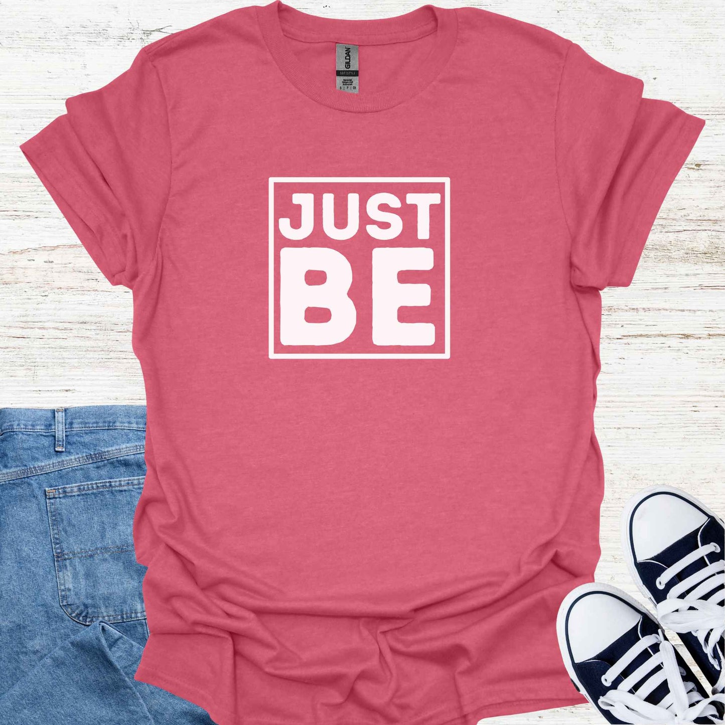 Red t-shirt design featuring the minimalist phrase 'Just Be' in bold typography, framed for emphasis. The design conveys a profound spiritual message about living in the present moment, embracing simplicity, and finding peace in existence itself. It encourages mindfulness, acceptance, and the art of simply being, free from the need to do or become anything. Perfect for those drawn to spirituality, introspection, and mindful living.