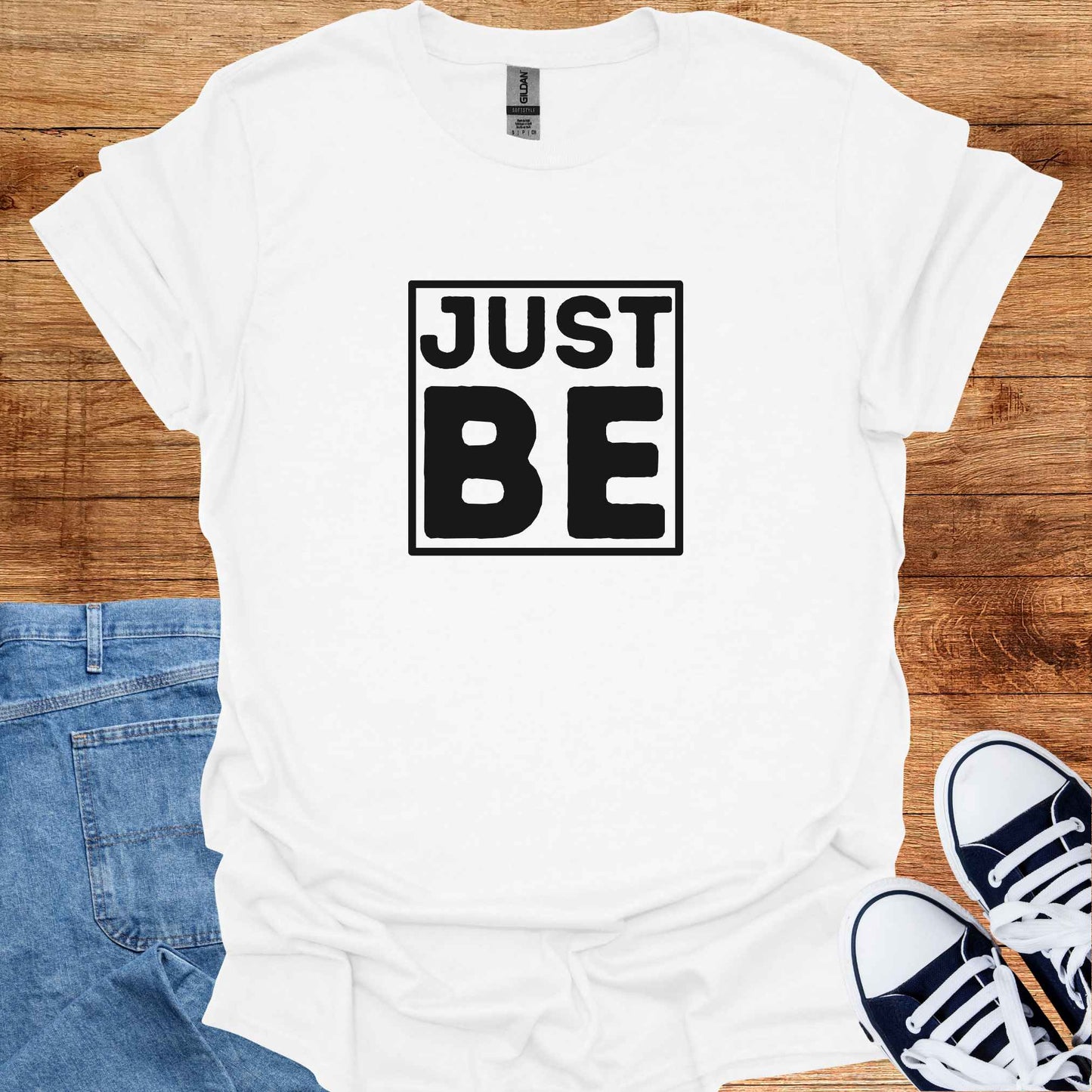 White t-shirt design featuring the minimalist phrase 'Just Be' in bold typography, framed for emphasis. The design conveys a profound spiritual message about living in the present moment, embracing simplicity, and finding peace in existence itself. It encourages mindfulness, acceptance, and the art of simply being, free from the need to do or become anything. Perfect for those drawn to spirituality, introspection, and mindful living.