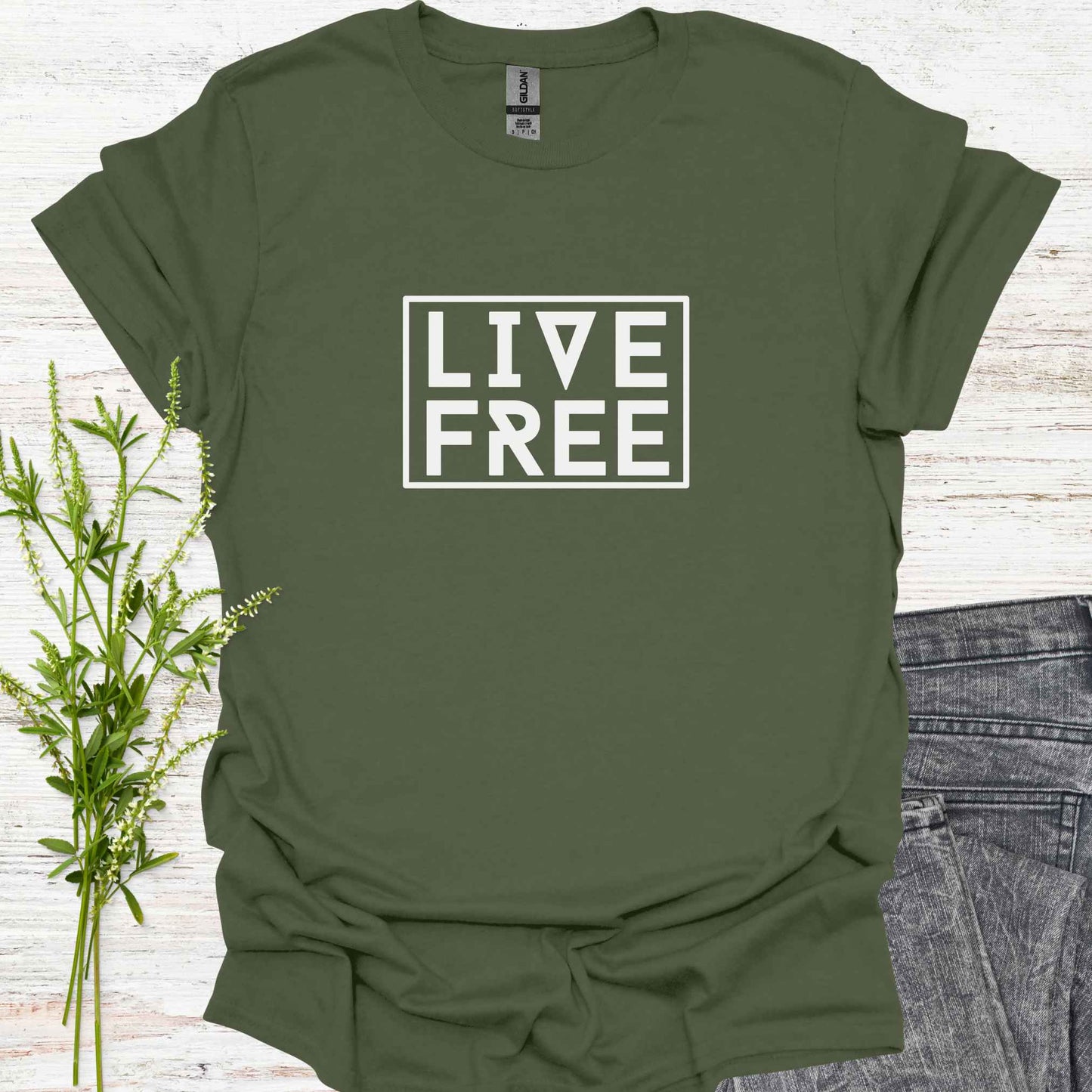 Military green t-shirt featuring bold text-based design with the phrase 'Live Free' framed on a minimalist background. This design embodies the spirit of independence, self-determination, and breaking free from mental constraints. It encourages a life aligned with personal values and freedom of thought, resonating with themes of spiritual liberation, individuality, and self-empowerment.
