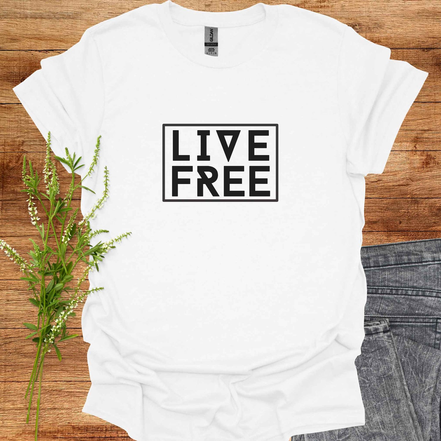 White t-shirt featuring bold text-based design with the phrase 'Live Free' framed on a minimalist background. This design embodies the spirit of independence, self-determination, and breaking free from mental constraints. It encourages a life aligned with personal values and freedom of thought, resonating with themes of spiritual liberation, individuality, and self-empowerment.