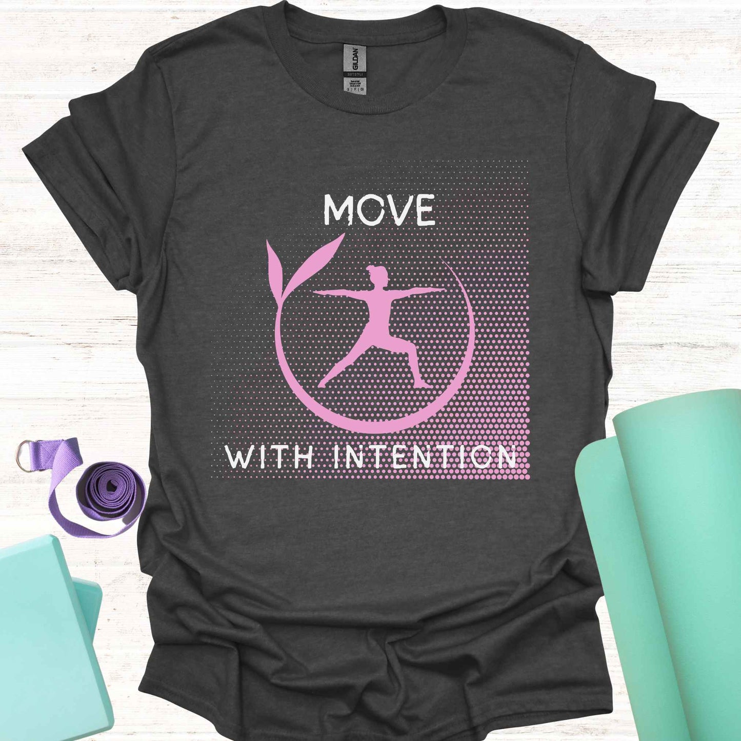 Dark grey t-shirt featuring a pink graphic of a figure in the yogic warrior pose, surrounded by a round frame, with the phrase 'Move with Intention.' This design embodies the central yoga teaching of mindfulness in every action, both on and off the mat. It encourages awareness, focus, and purpose in all movements, promoting balance, strength, and conscious living.