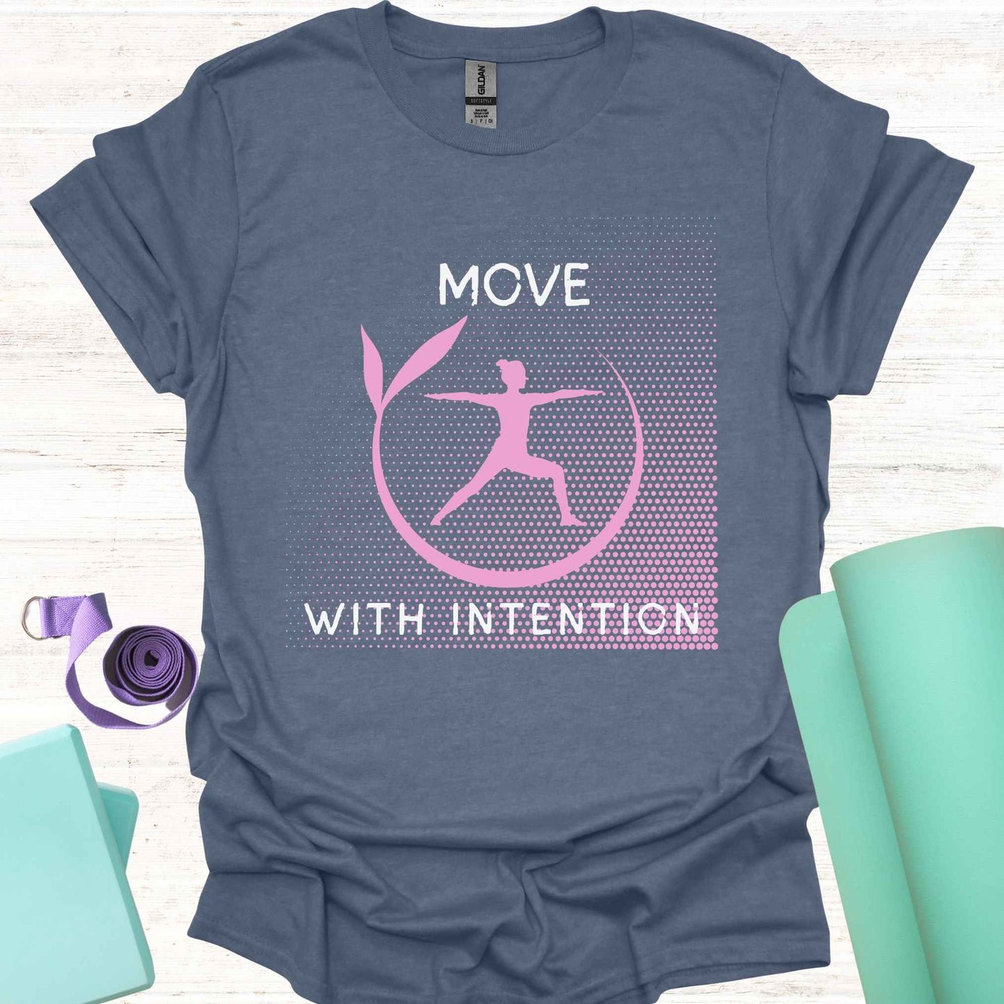 Blue t-shirt featuring a pink graphic of a figure in the yogic warrior pose, surrounded by a round frame, with the phrase 'Move with Intention.' This design embodies the central yoga teaching of mindfulness in every action, both on and off the mat. It encourages awareness, focus, and purpose in all movements, promoting balance, strength, and conscious living.