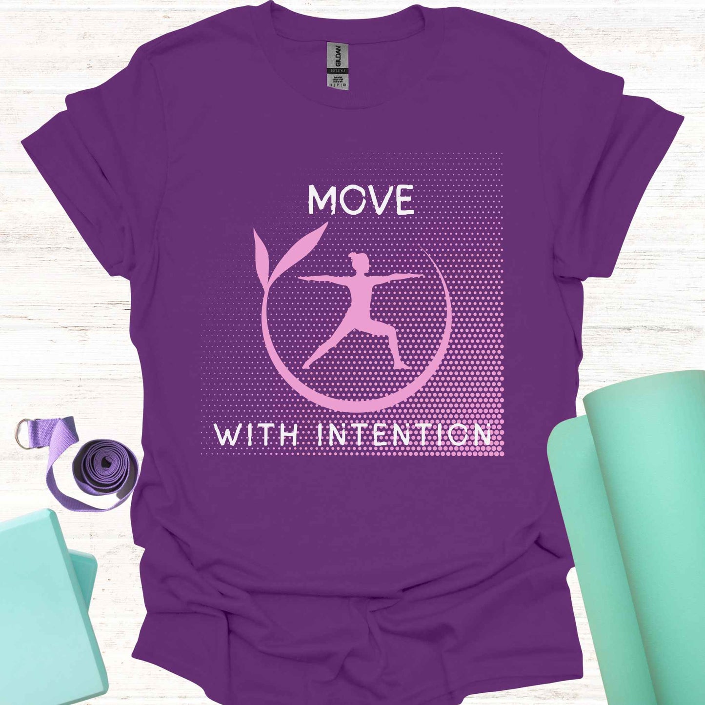 Purple t-shirt featuring a pink graphic of a figure in the yogic warrior pose, surrounded by a round frame, with the phrase 'Move with Intention.' This design embodies the central yoga teaching of mindfulness in every action, both on and off the mat. It encourages awareness, focus, and purpose in all movements, promoting balance, strength, and conscious living.