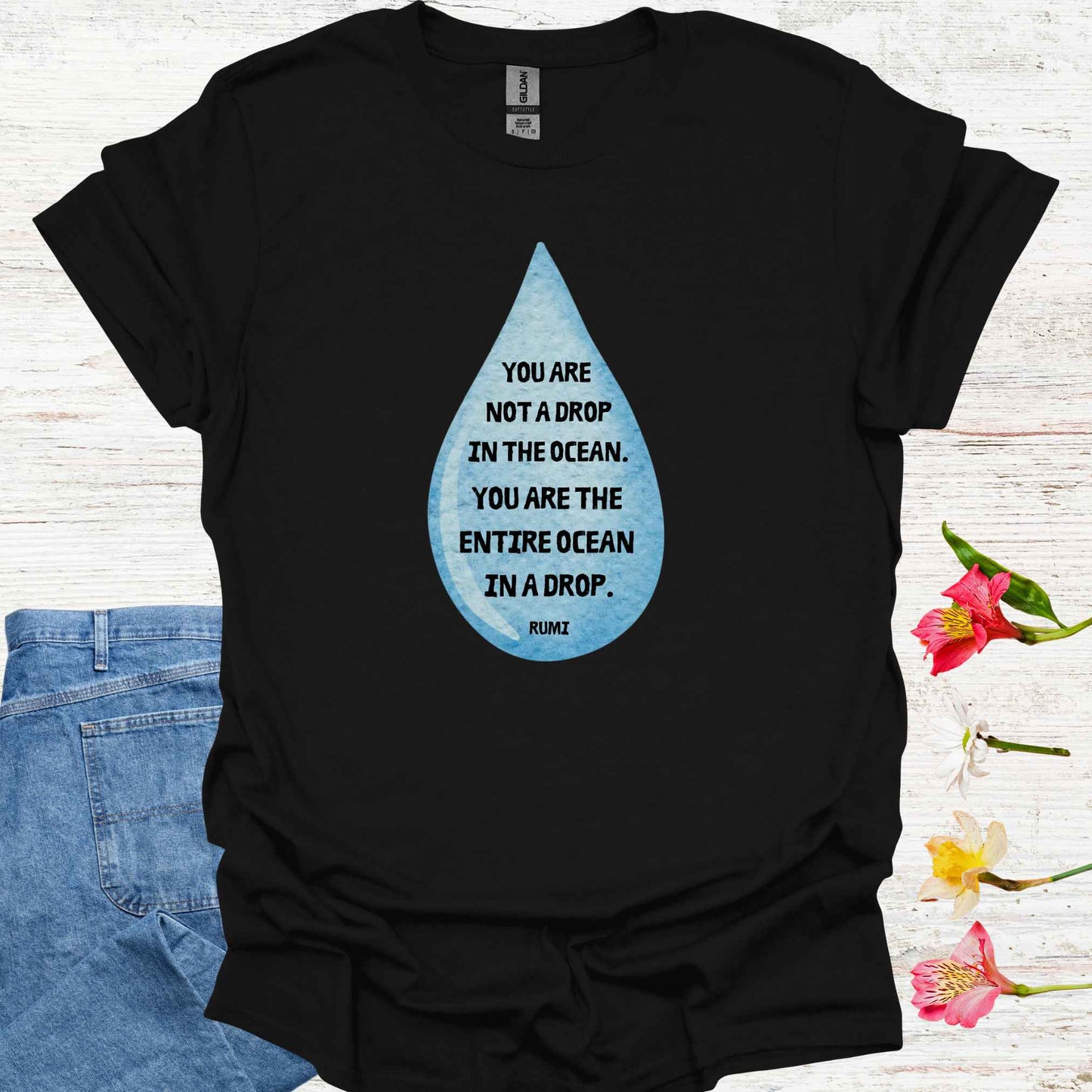 Black t-shirt featuring design of a watercolor blue drop with the profound Rumi quote: "You are not a drop in the ocean. You are the entire ocean in a drop." The words are elegantly printed within the drop, emphasizing the metaphor of universal consciousness residing within each individual. This design symbolizes the non-dual nature of existence, reminding spiritual seekers and meditators of the infinite potential and interconnectedness within all.