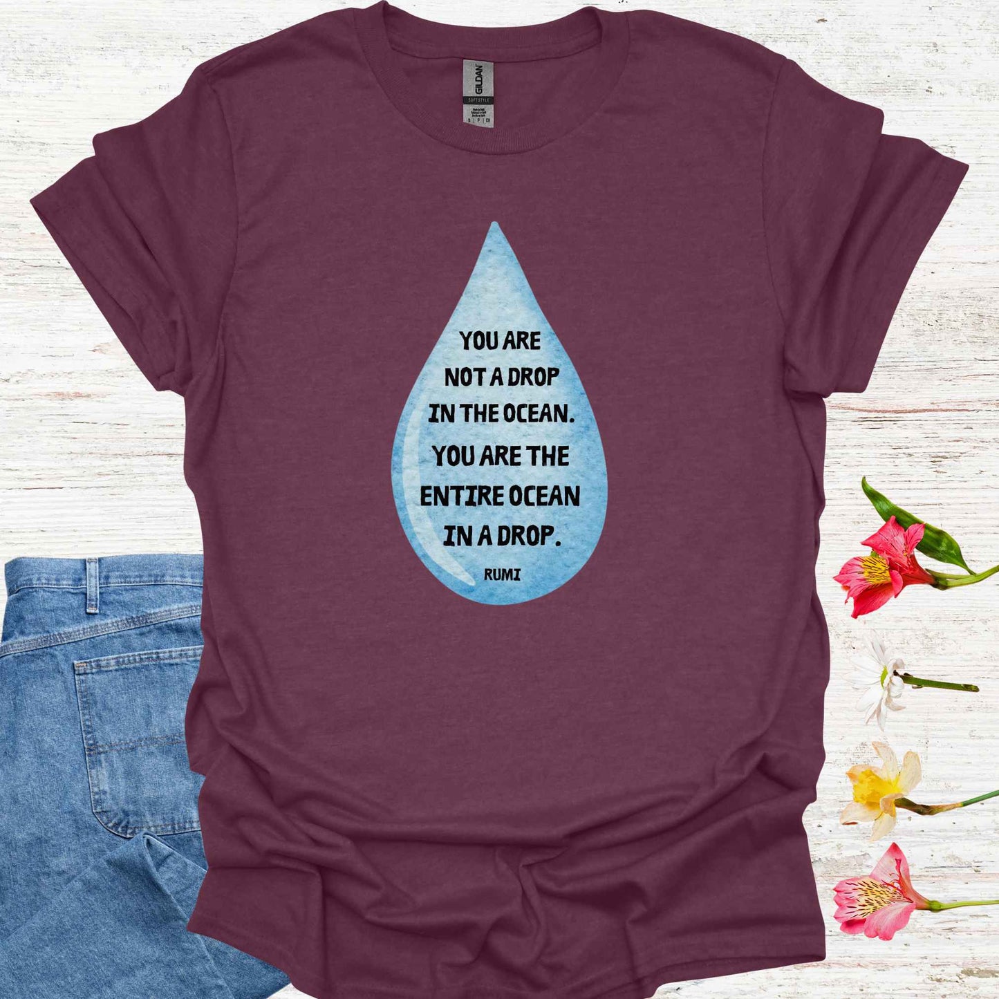 Maroon purple t-shirt featuring design of a watercolor blue drop with the profound Rumi quote: "You are not a drop in the ocean. You are the entire ocean in a drop." The words are elegantly printed within the drop, emphasizing the metaphor of universal consciousness residing within each individual. This design symbolizes the non-dual nature of existence, reminding spiritual seekers and meditators of the infinite potential and interconnectedness within all.
