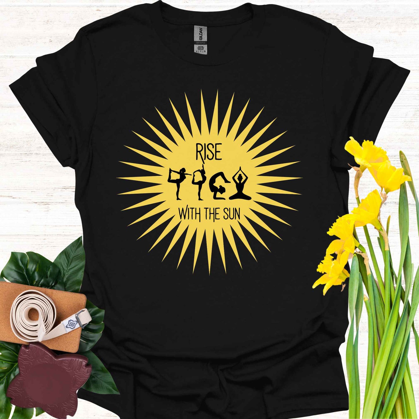 Black t-shirt featuring a bright yellow sun graphic, with human forms in various yoga poses placed within the sun’s rays. The design is accompanied by the phrase 'Rise with the Sun,' symbolizing the connection between yoga, movement, and the natural rhythm of the day. This design encourages wearers to embrace vitality, inner balance, and strength, making it perfect for yoga practitioners and those seeking inspiration from both nature and mindful movement.