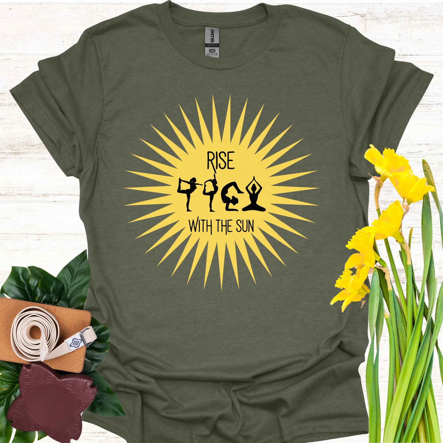 Green t-shirt featuring a bright yellow sun graphic, with human forms in various yoga poses placed within the sun’s rays. The design is accompanied by the phrase 'Rise with the Sun,' symbolizing the connection between yoga, movement, and the natural rhythm of the day. This design encourages wearers to embrace vitality, inner balance, and strength, making it perfect for yoga practitioners and those seeking inspiration from both nature and mindful movement.