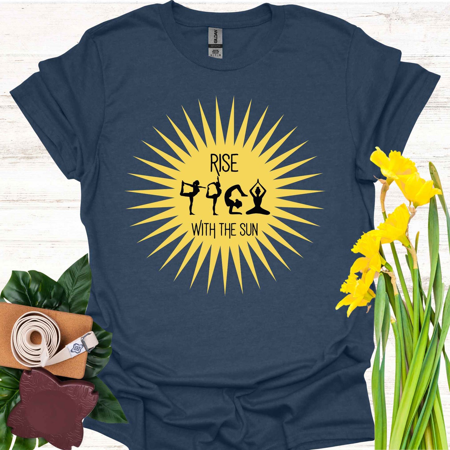 Navy blue t-shirt featuring a bright yellow sun graphic, with human forms in various yoga poses placed within the sun’s rays. The design is accompanied by the phrase 'Rise with the Sun,' symbolizing the connection between yoga, movement, and the natural rhythm of the day. This design encourages wearers to embrace vitality, inner balance, and strength, making it perfect for yoga practitioners and those seeking inspiration from both nature and mindful movement.