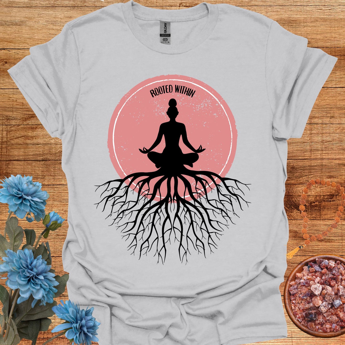 Grey t-shirt featuring a graphic of deep tree roots extending downward, with the form of a meditating person sitting on top, suggesting that the roots belong to the meditator. This design symbolizes the yogic teaching of keeping awareness within, grounding oneself in inner peace, and embodying wisdom through meditation and spiritual practice.