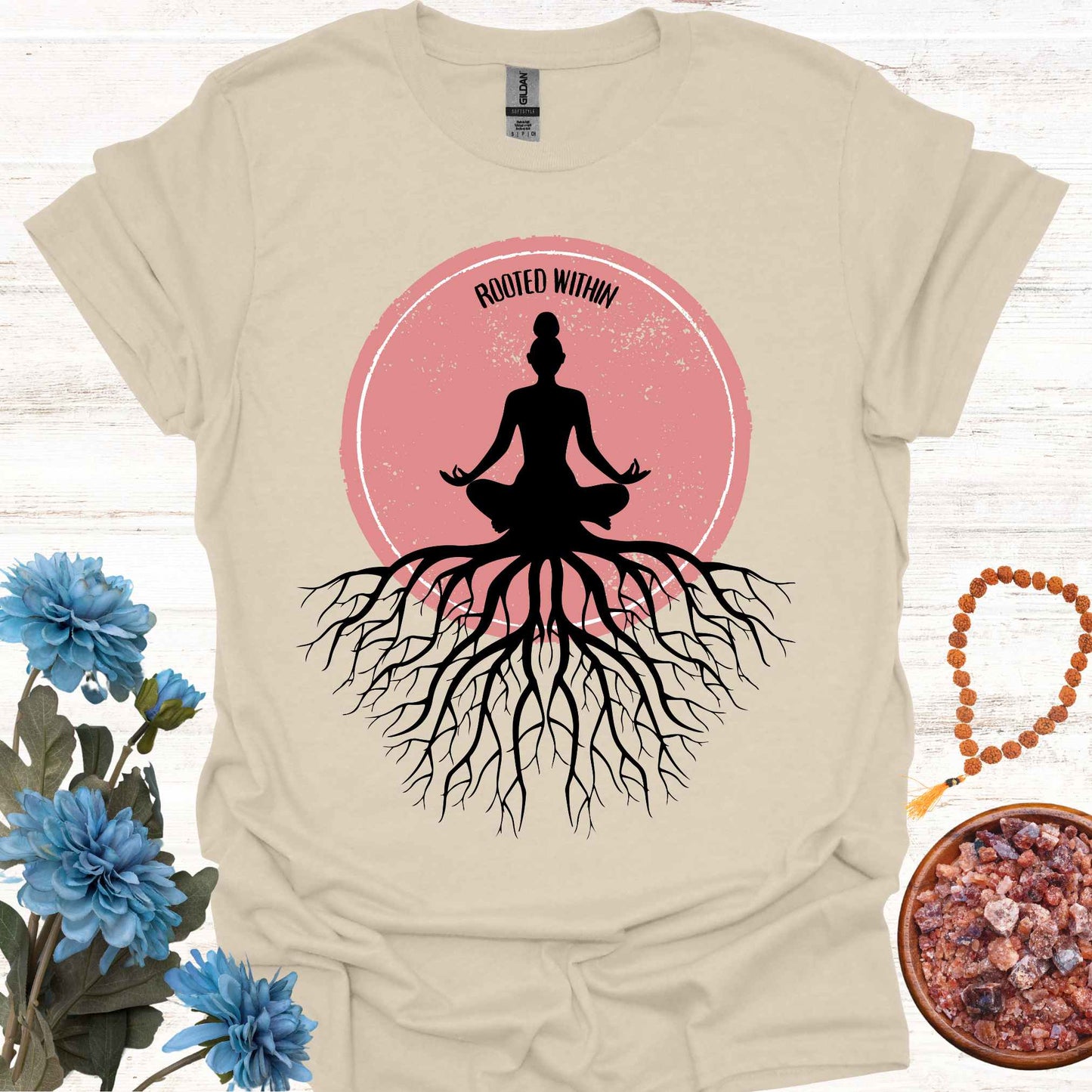 Beige t-shirt featuring a graphic of deep tree roots extending downward, with the form of a meditating person sitting on top, suggesting that the roots belong to the meditator. This design symbolizes the yogic teaching of keeping awareness within, grounding oneself in inner peace, and embodying wisdom through meditation and spiritual practice