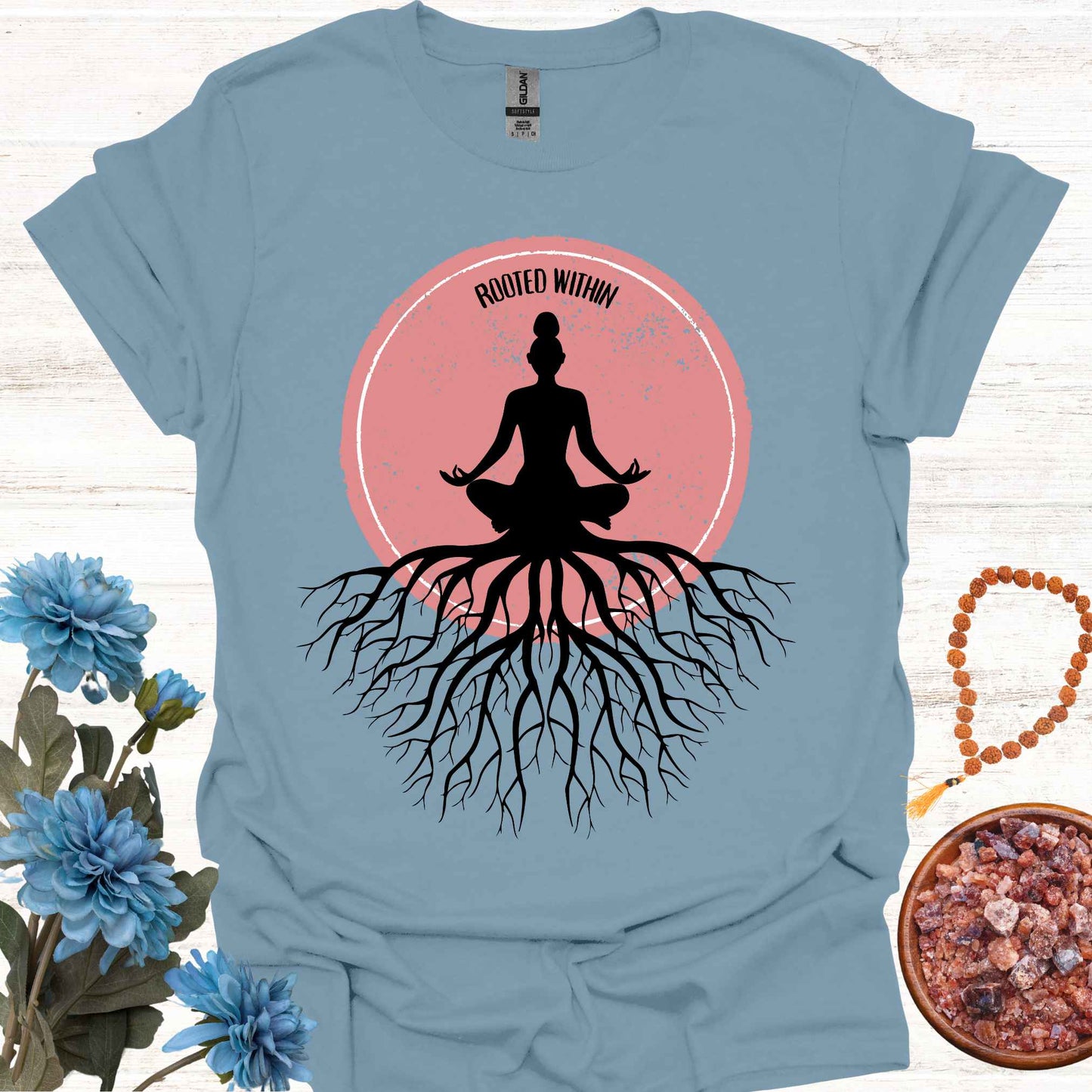 Blue t-shirt featuring a graphic of deep tree roots extending downward, with the form of a meditating person sitting on top, suggesting that the roots belong to the meditator. This design symbolizes the yogic teaching of keeping awareness within, grounding oneself in inner peace, and embodying wisdom through meditation and spiritual practice