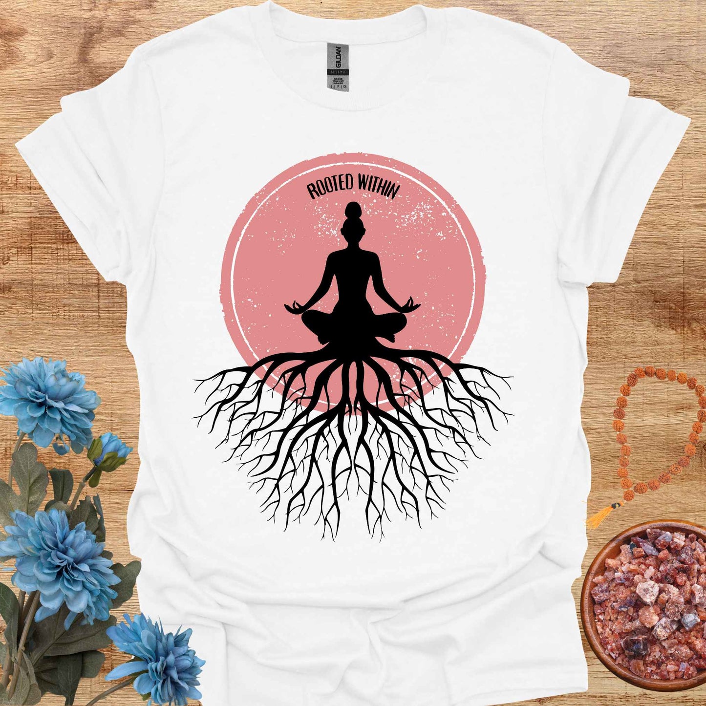 White t-shirt featuring a graphic of deep tree roots extending downward, with the form of a meditating person sitting on top, suggesting that the roots belong to the meditator. This design symbolizes the yogic teaching of keeping awareness within, grounding oneself in inner peace, and embodying wisdom through meditation and spiritual practice