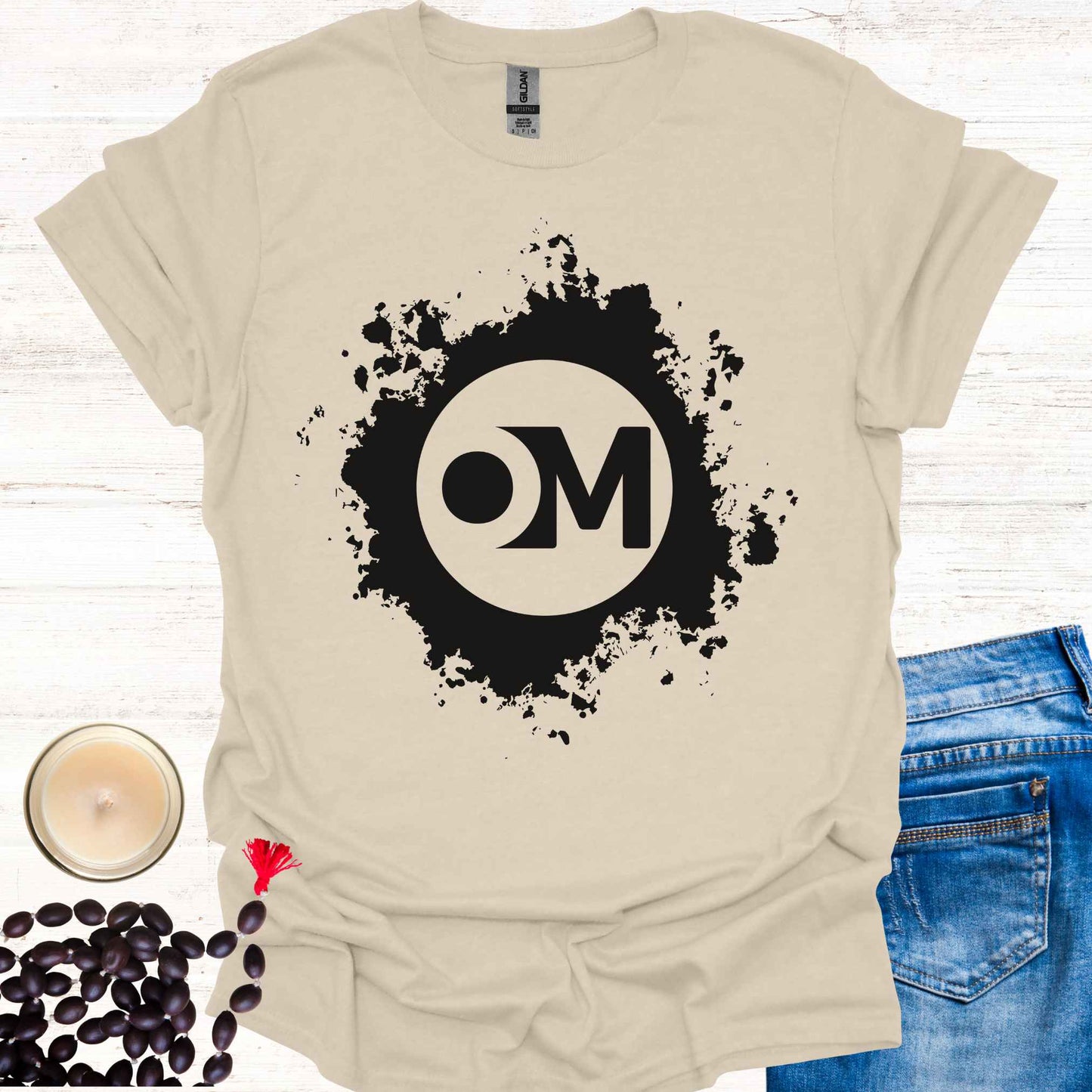 Beige t-shirt featuring the word 'OM' at the center of a black abstract graphic. Om is a sacred sound and symbol representing universal vibration, interconnectedness, and divine energy. This design invites inner peace, mindfulness, and spiritual harmony, ideal for meditators and yogis.