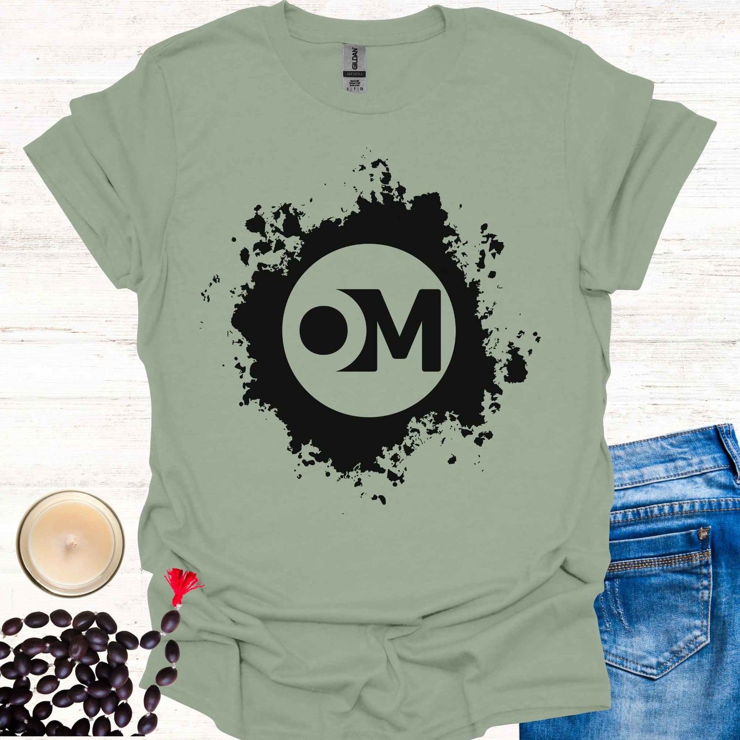 Sage green t-shirt featuring the word 'OM' at the center of a black abstract graphic. Om is a sacred sound and symbol representing universal vibration, interconnectedness, and divine energy. This design invites inner peace, mindfulness, and spiritual harmony, ideal for meditators and yogis.