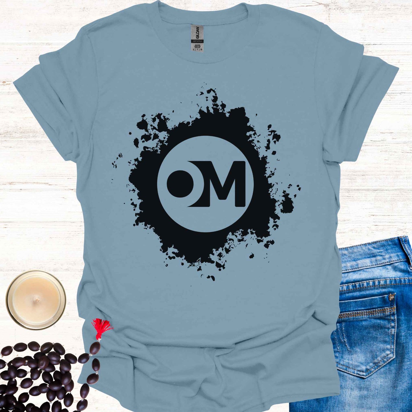 Blue t-shirt featuring the word 'OM' at the center of a black abstract graphic. Om is a sacred sound and symbol representing universal vibration, interconnectedness, and divine energy. This design invites inner peace, mindfulness, and spiritual harmony, ideal for meditators and yogis.