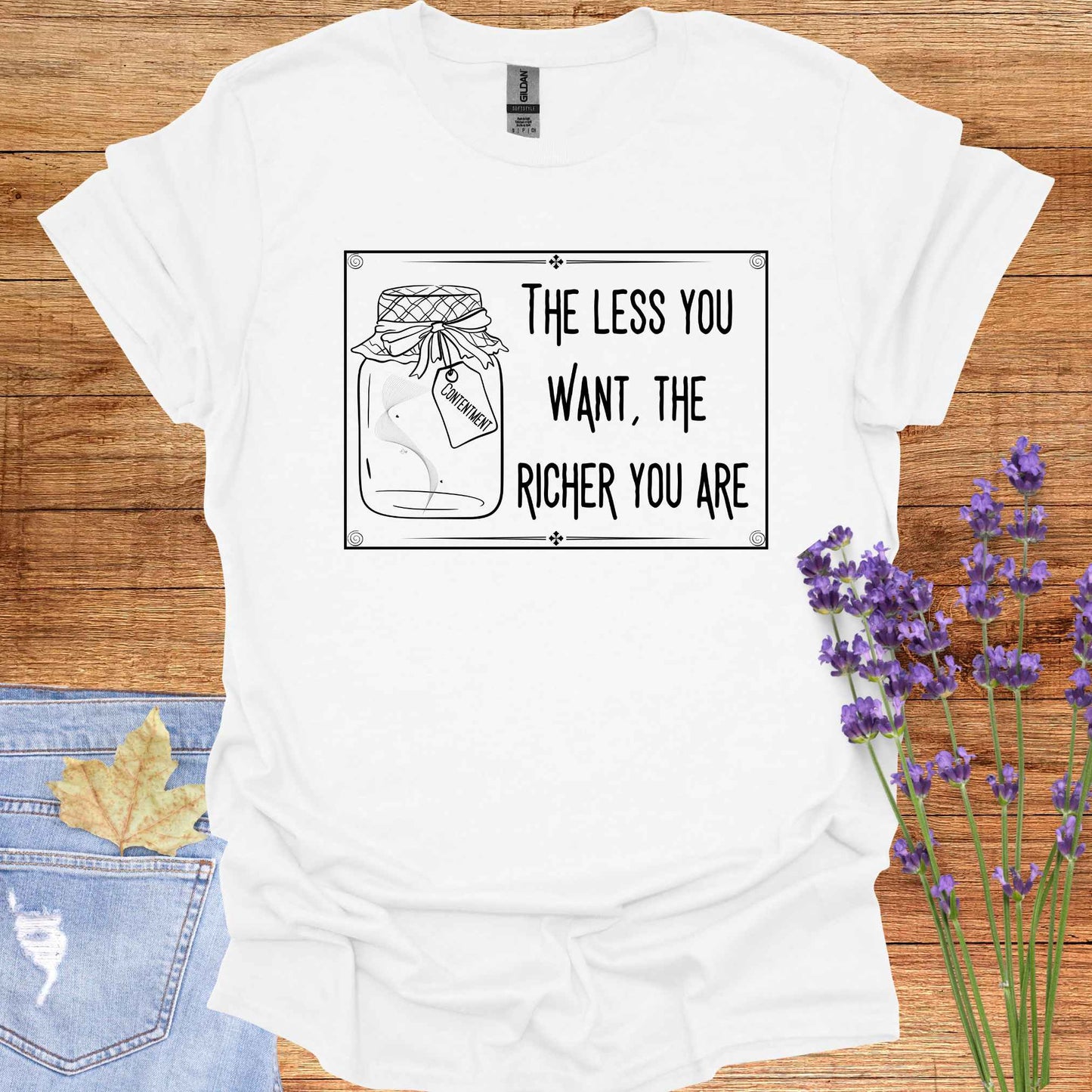 White t-shirt featuring a framed black-and-white graphic of an empty jar labelled 'Contentment,' paired with the minimalist phrase 'The Less You Want, The Richer You Are.' This design symbolizes detachment, inner fulfillment, and the spiritual ideal of finding inner richness through desirelessness.
