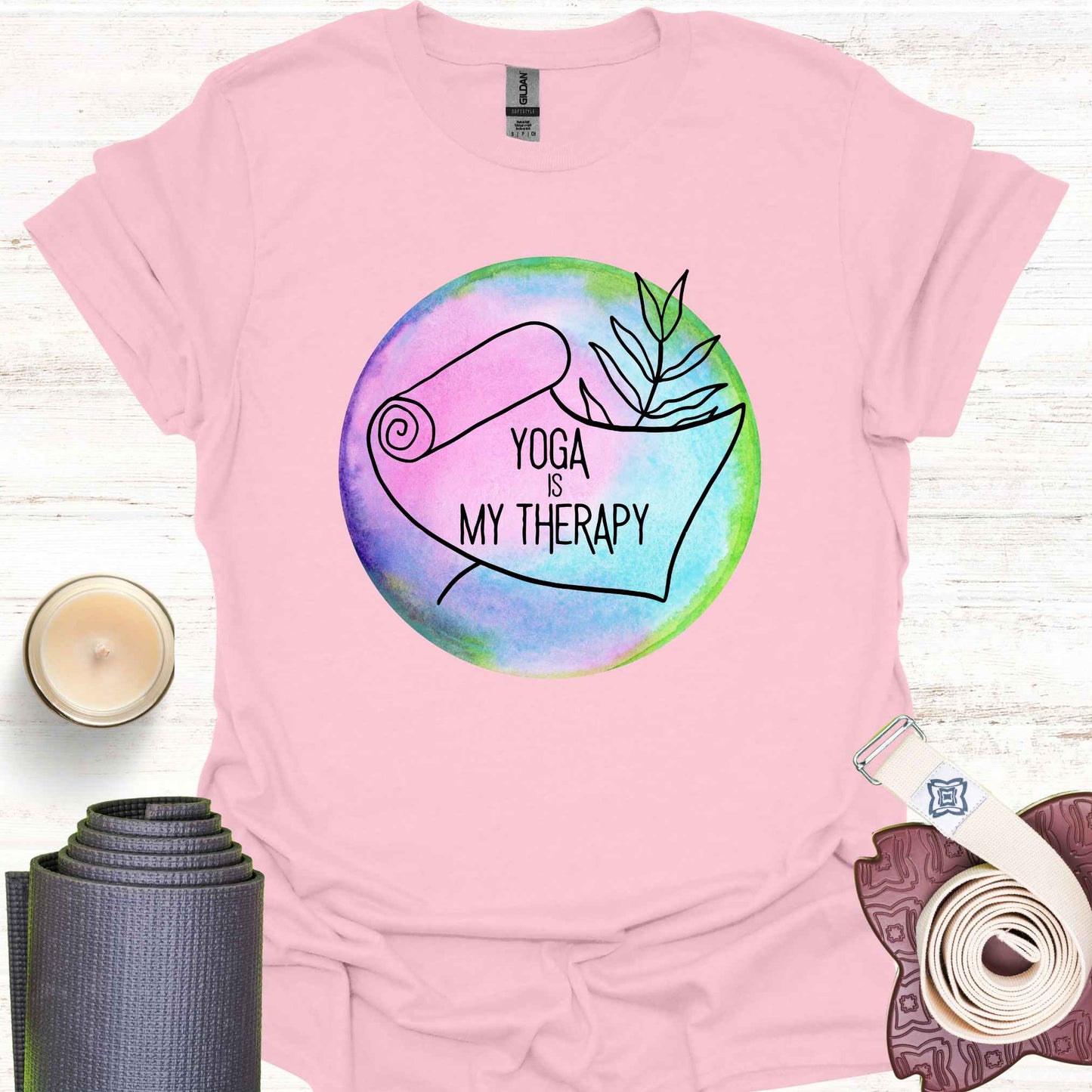 Light pink t-shirt featuring a graphic of a yoga mat placed on a round, colorful watercolour background, with the phrase 'Yoga is My Therapy.' This design highlights the therapeutic power of yoga, promoting physical and mental well-being, relaxation, and mindfulness. Perfect for those who turn to yoga as a form of self-care, stress relief, and personal healing.