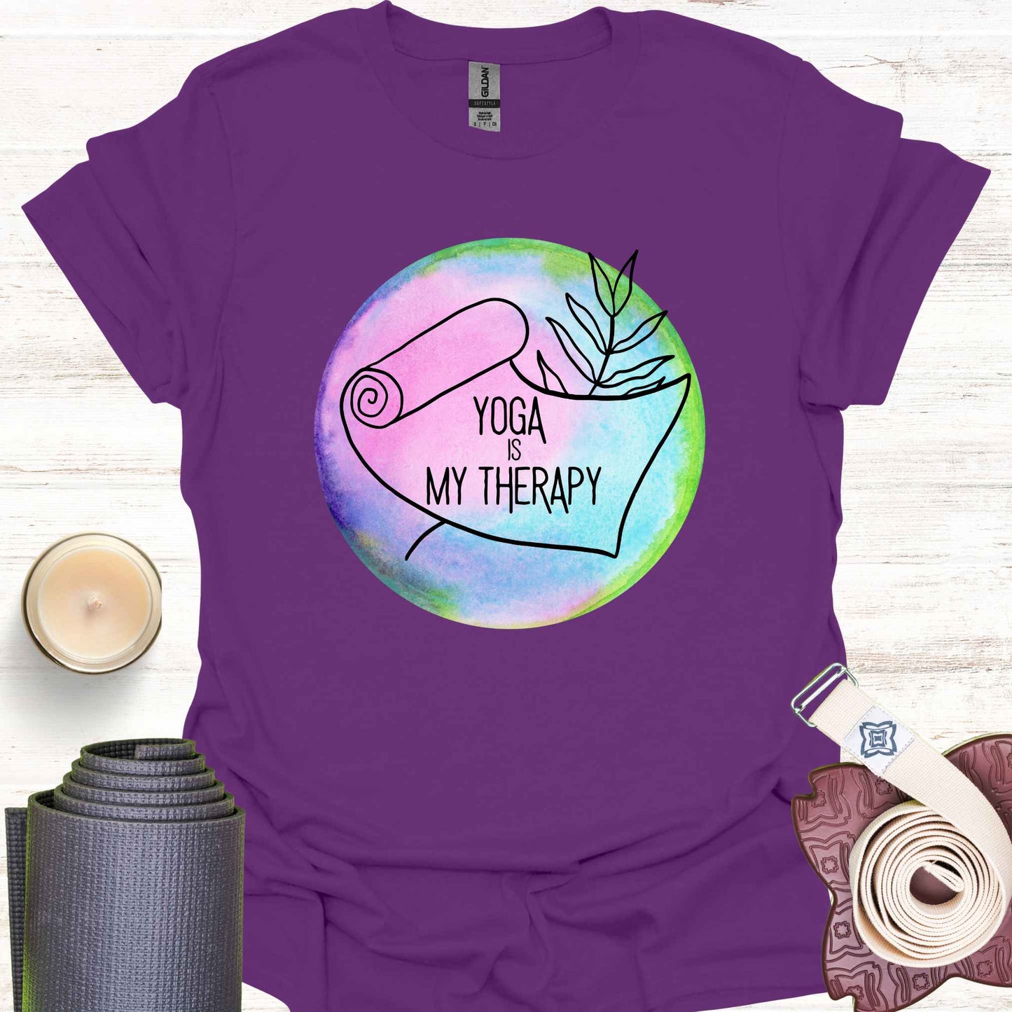 Purple t-shirt featuring a graphic of a yoga mat placed on a round, colorful watercolour background, with the phrase 'Yoga is My Therapy.' This design highlights the therapeutic power of yoga, promoting physical and mental well-being, relaxation, and mindfulness. Perfect for those who turn to yoga as a form of self-care, stress relief, and personal healing.