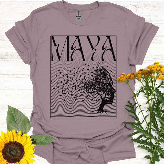 Light purple t-shirt featuring the word 'Maya' above an optical illusion graphic of a tree shaped like a face, with leaves blowing in the wind and an abstract wavy background pattern. The design symbolizes the Sanskrit concept of 'maya,' meaning illusion, highlighting the illusory nature of reality shaped by the mind. It evokes themes of duality, self-reflection, and the power of thought in creating our perceptions, encouraging deeper awareness and questioning of assumptions about reality.