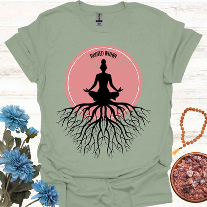 Sage green t-shirt featuring a graphic of deep tree roots extending downward, with the form of a meditating person sitting on top, suggesting that the roots belong to the meditator. This design symbolizes the yogic teaching of keeping awareness within, grounding oneself in inner peace, and embodying wisdom through meditation and spiritual practice.